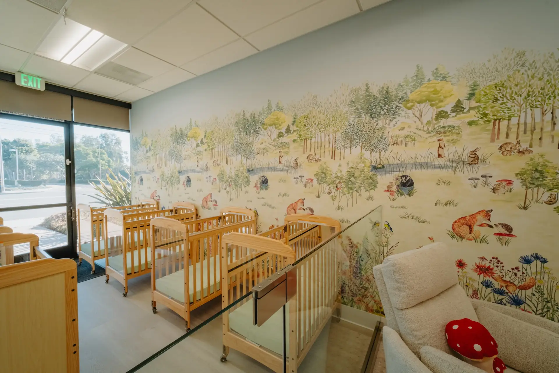 Infant room with woodland mural and cribs at Ohana Montessori
